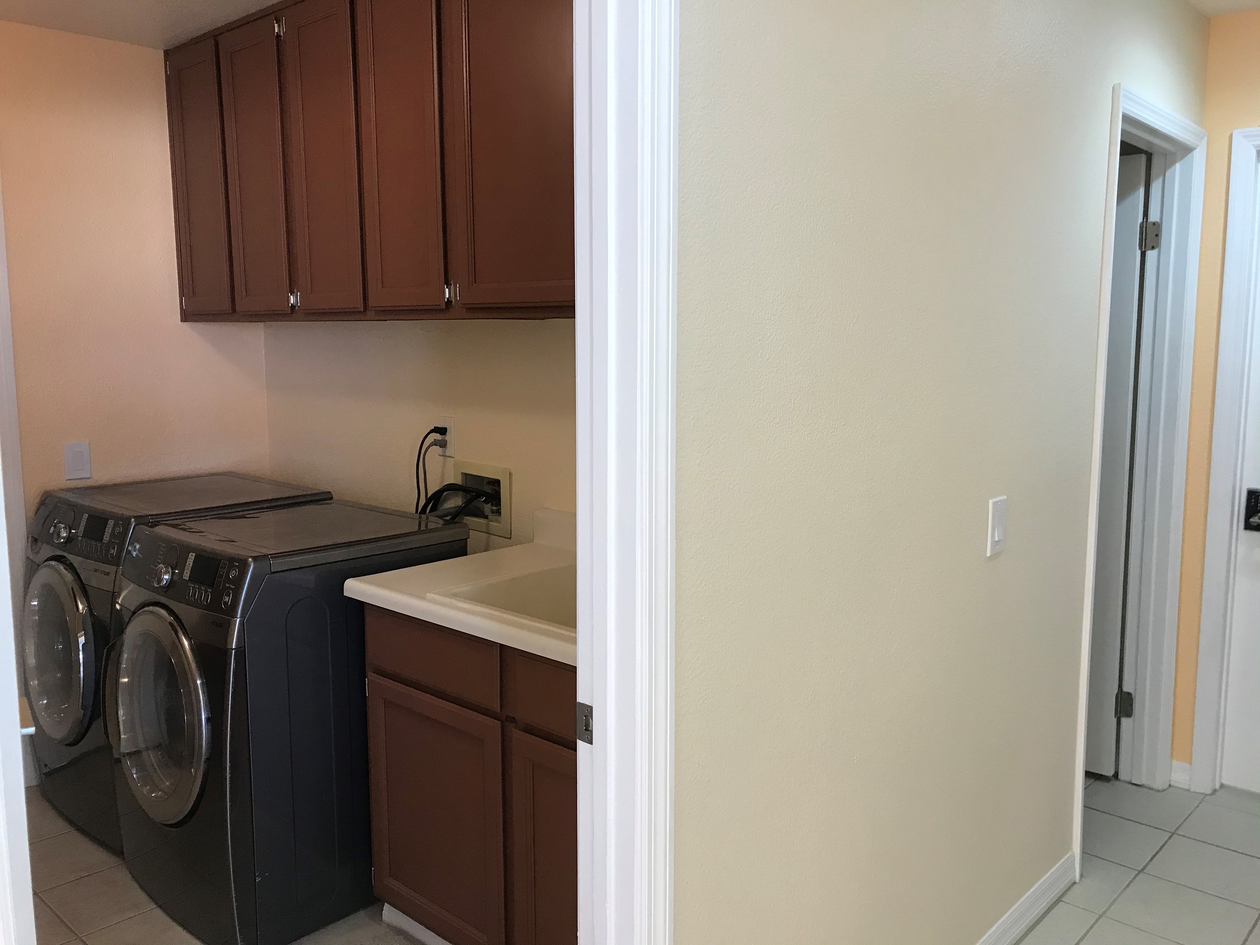 Full-size front-load washer and dryer with rich wood cabinetry and utility sink