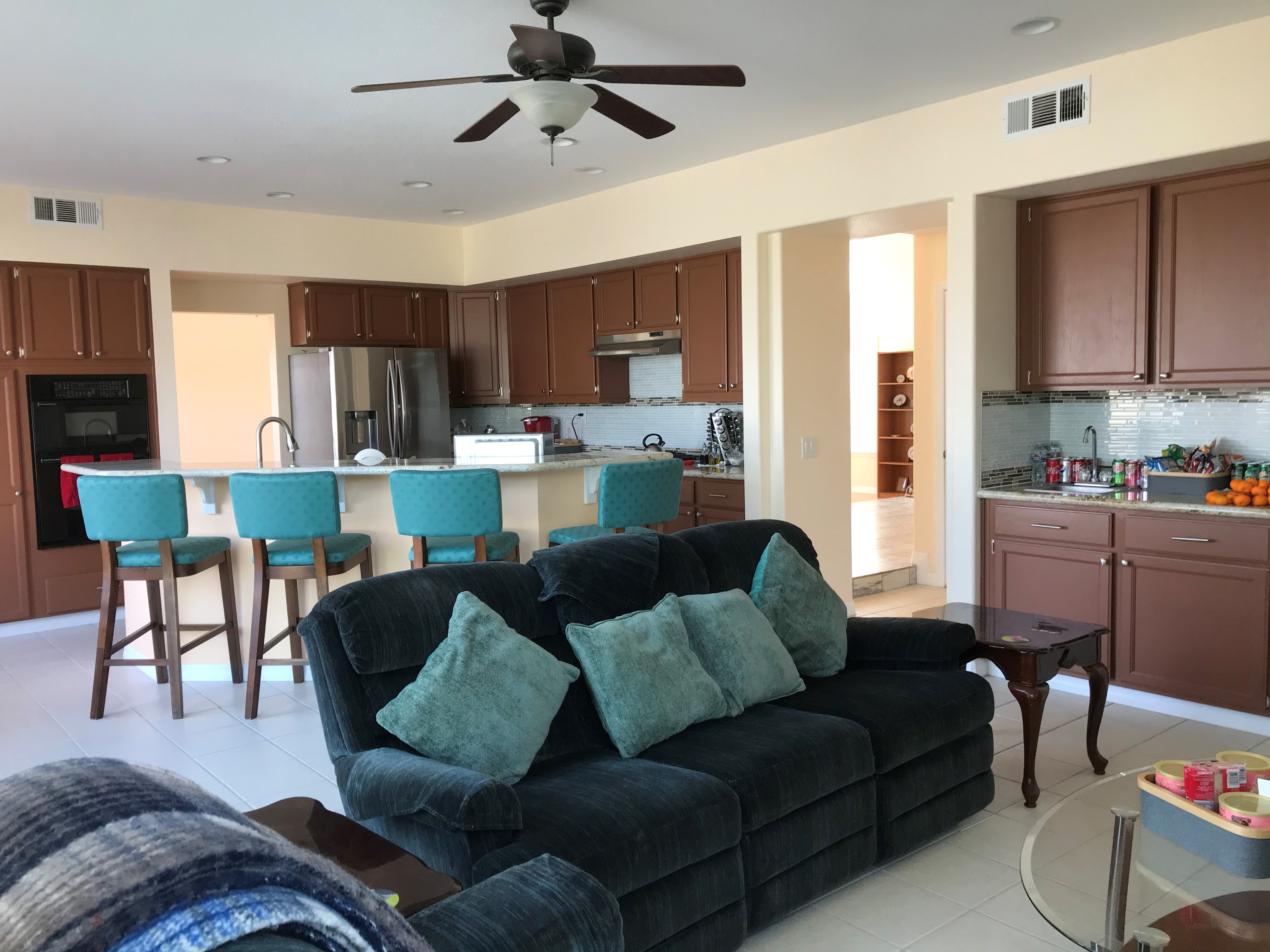 Open-concept kitchen and family room with teal bar stools, granite island, and stainless steel appliances